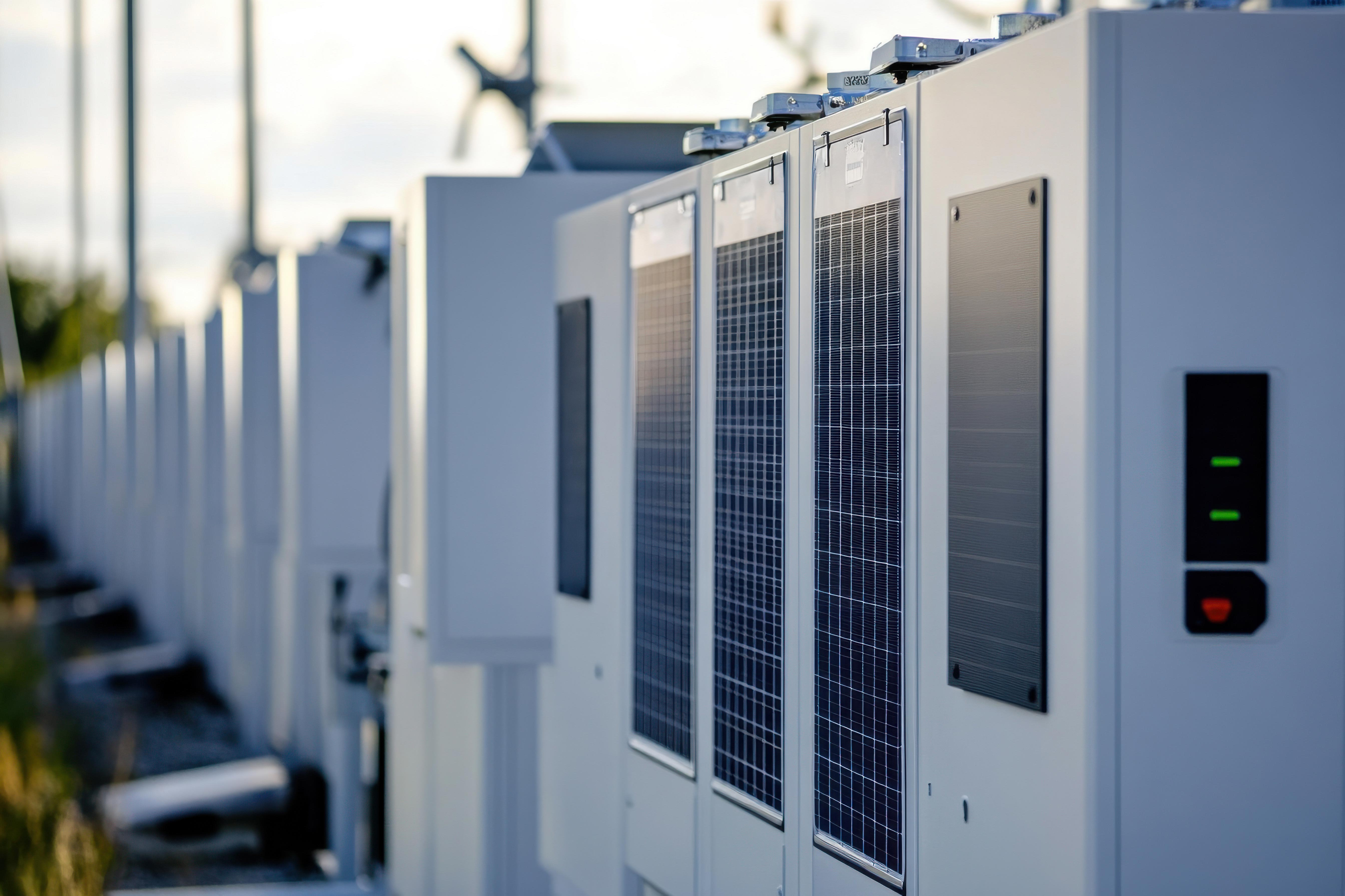 Fila de acumuladores de energia brancos ao ar livre ao pôr do sol; infraestrutura energética moderna.